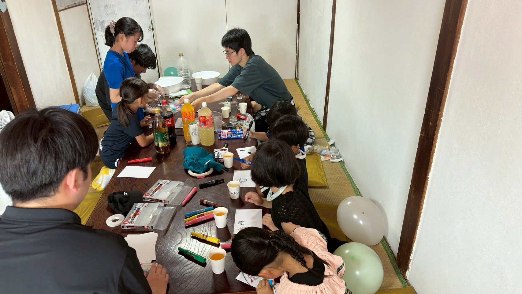 テーブルを囲み、お絵描きに夢中になる子どもたちと学生スタッフ