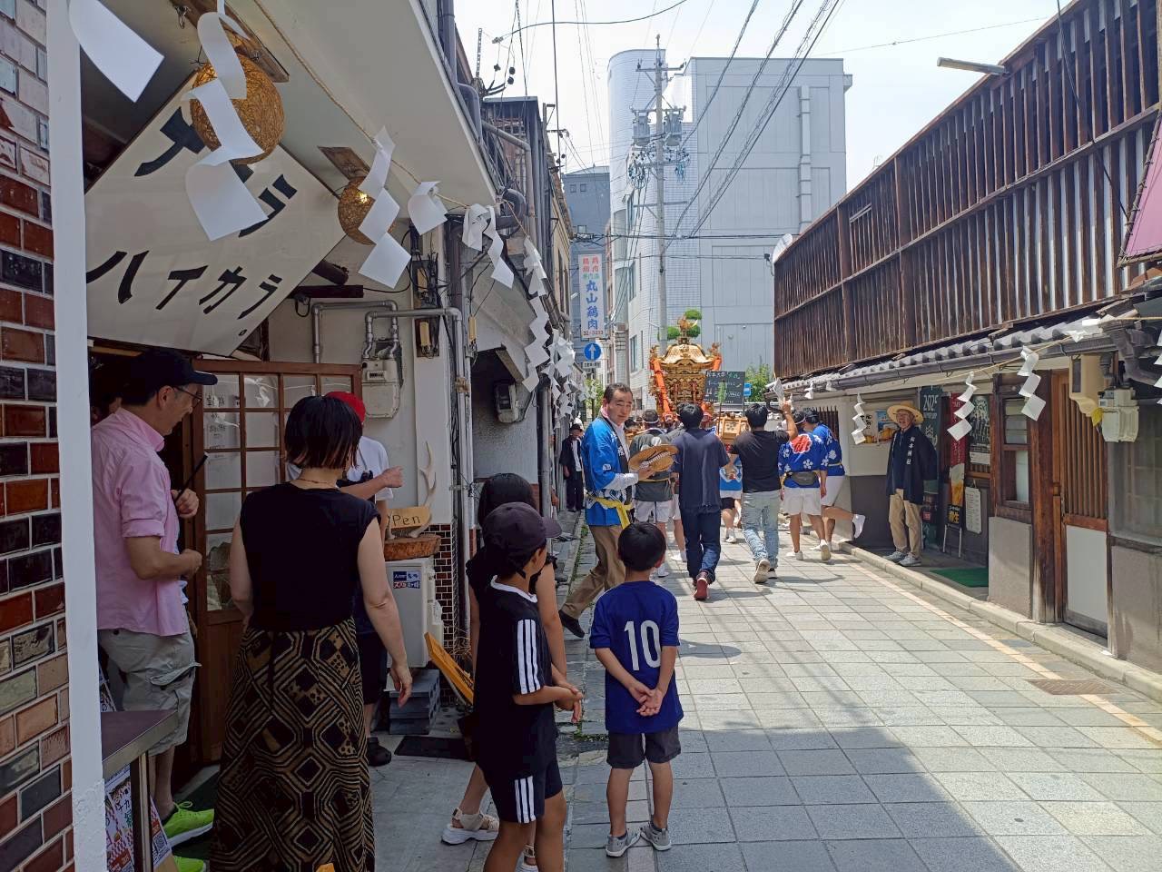 紙垂が飾られたナカラハイカラの店先を、神輿が通り過ぎていく上土通り