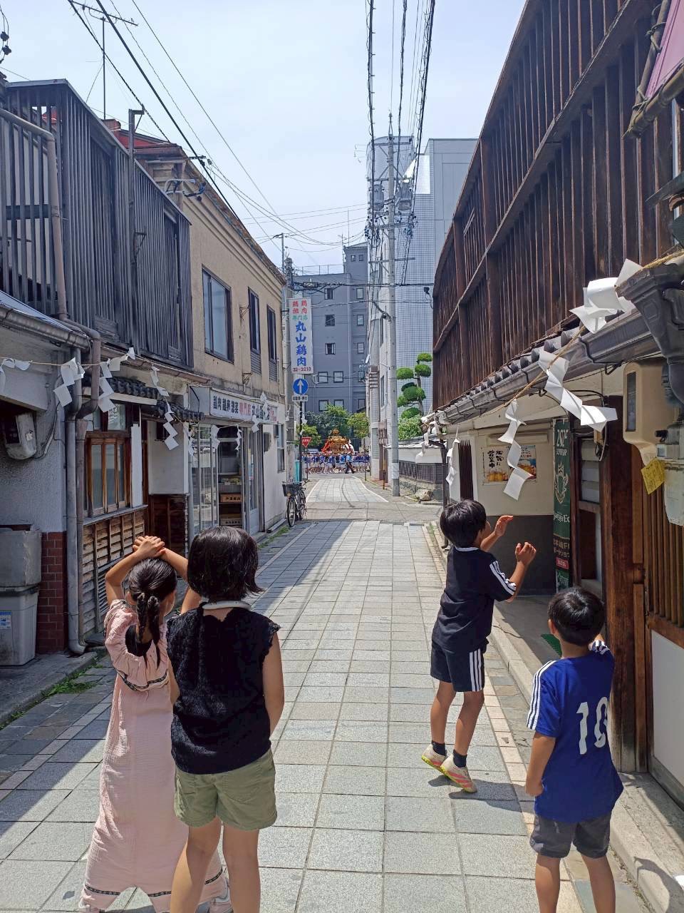 紙垂の下がる路地の先、神輿が来るのを背伸びして待つ子どもたち